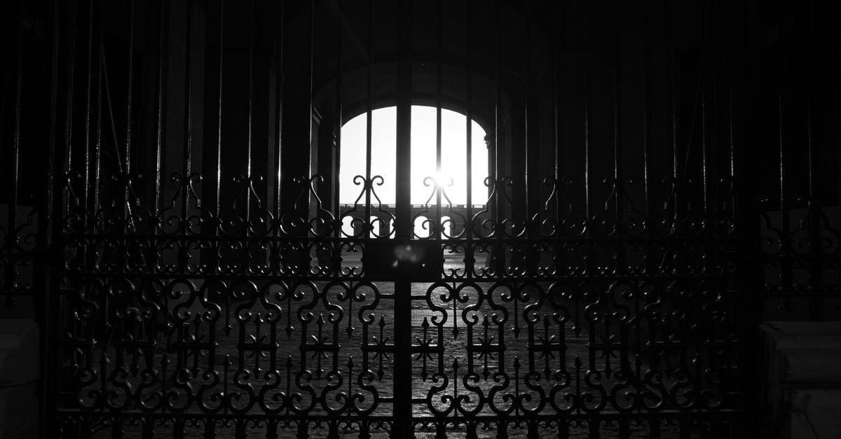 Black and white silhouette of an ornate iron gate with architectural details.